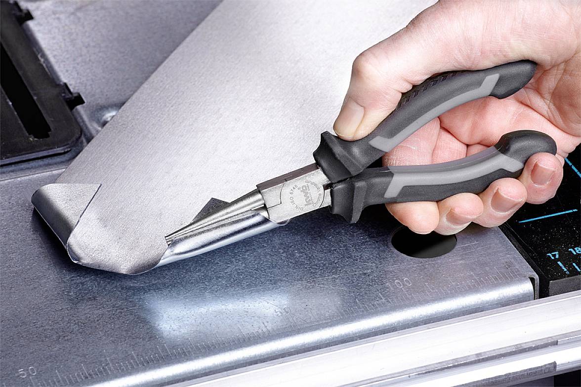 A hand holds pliers and shapes a piece of metal on a workbench.