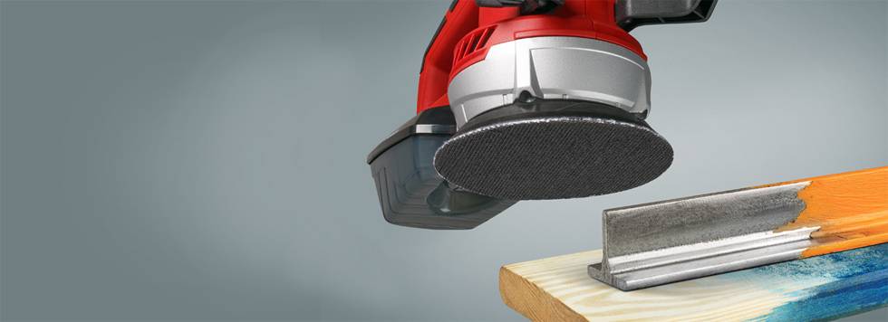 A red grinding machine is sanding the corner of a wooden beam, with a metal angle bracket being used for stabilisation.