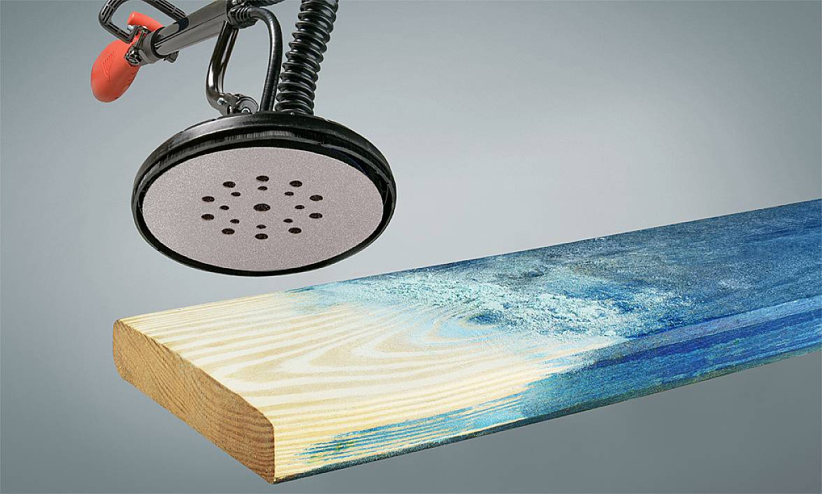 A sander removes blue paint from a piece of wood to reveal its original grain.
