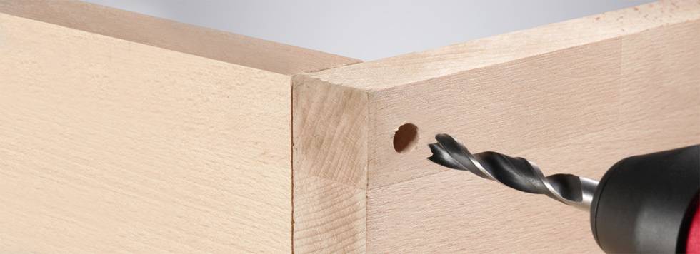 A drill precisely bores into a wooden edge, creating a hole for assembly, captured in close-up.