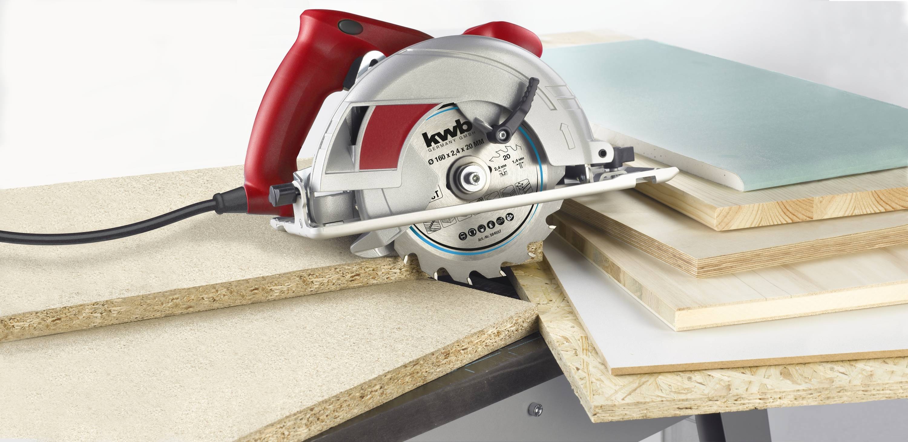 A circular hand saw with a red handle cuts through several wooden boards of different types and thicknesses.