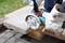A person wearing gloves is using an electric cutting disc to cut a concrete slab on wooden blocks.