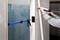 A person is securing a white trim with a caulking gun at the edge of a wall. A clamp is holding the trim in position.