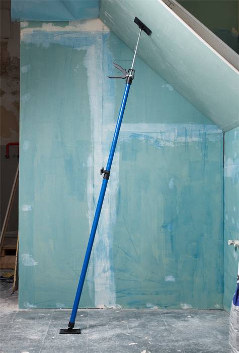 A blue telescopic support prop is bracing a slanted, green-plastered wall in a room with a construction site atmosphere.