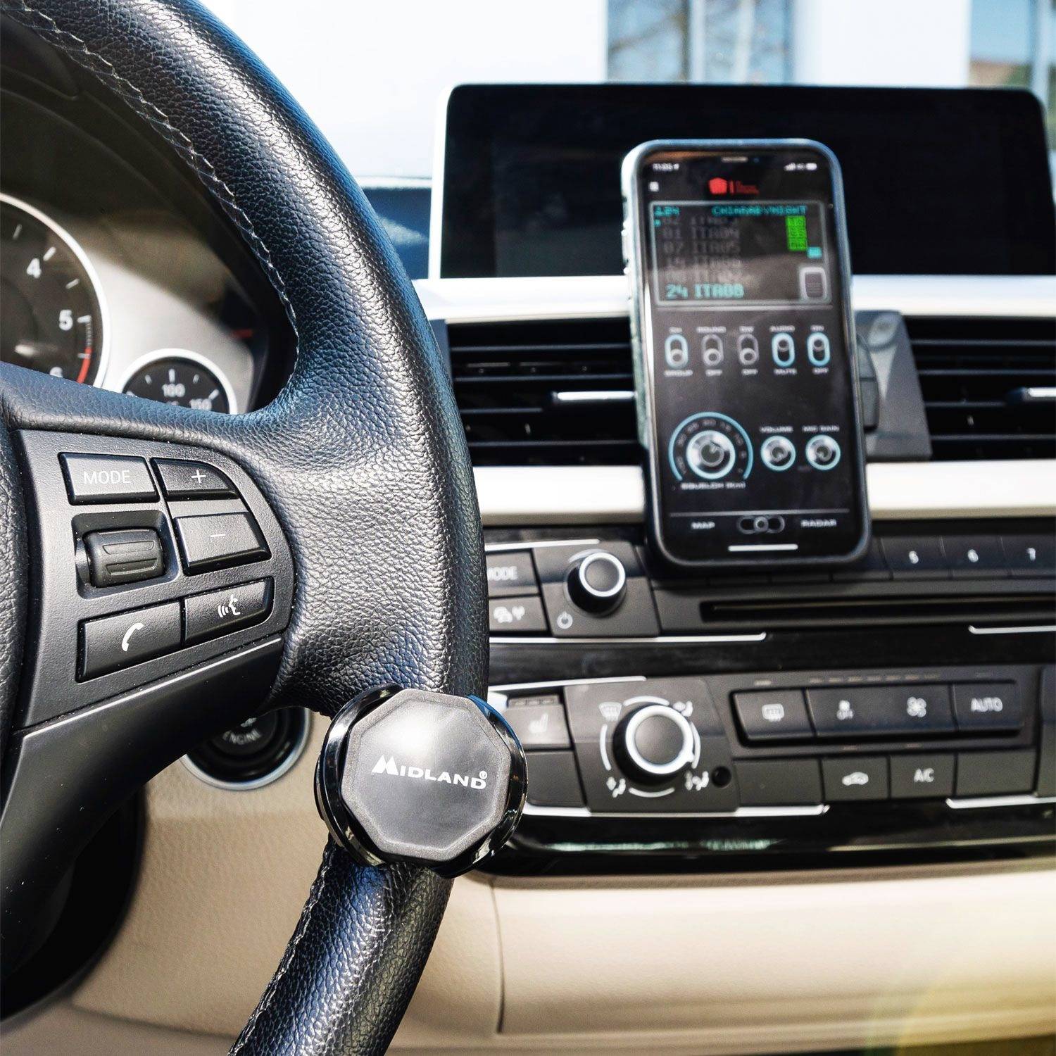 A smartphone is mounted in a car holder on the dashboard, with a driver's view of the steering wheel of a vehicle.