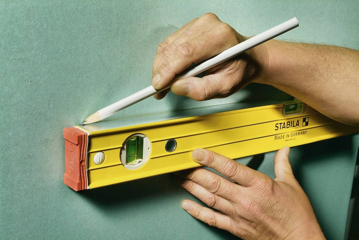 A person is holding a yellow spirit level against a green wall and marking a line with a white pencil.