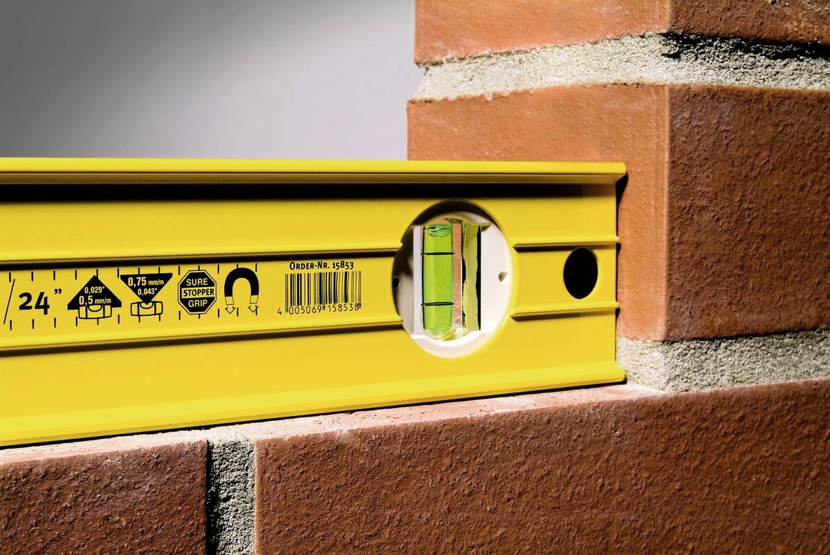 A yellow spirit level indicates that a brick wall is level. It lies horizontally along the edge of the wall.