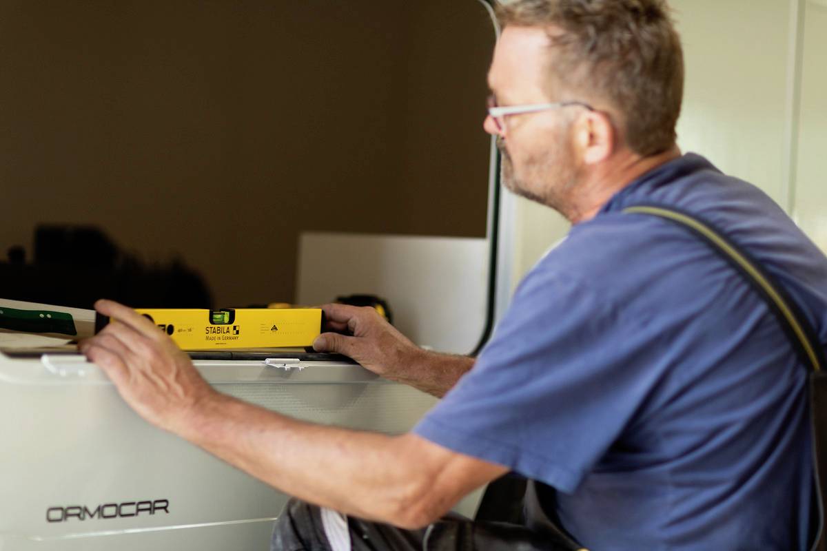 A man is checking the alignment of a white rectangular object with a spirit level. He is wearing a blue T-shirt and glasses.