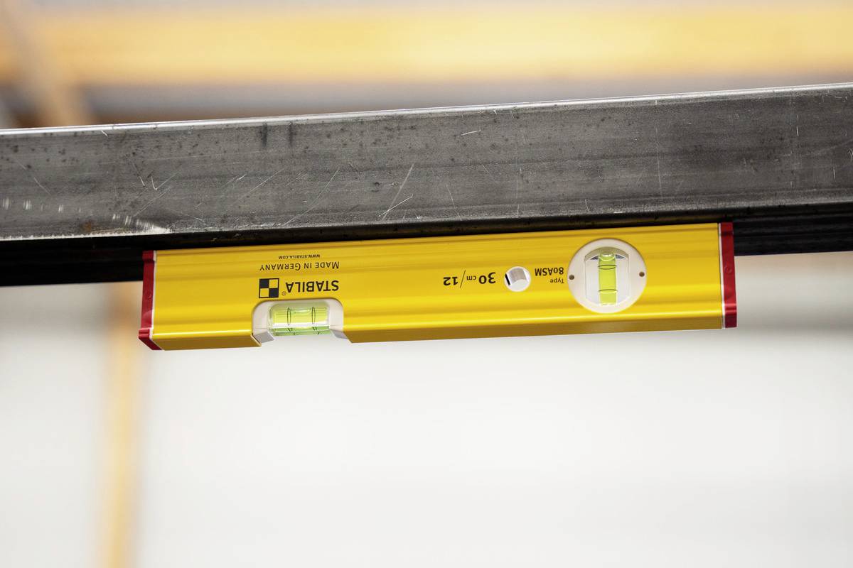 A yellow spirit level is lying horizontally on a steel beam with a slightly off-centre air bubble in the sight glass.