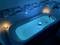 A filled bathtub illuminated by soft, blue light with candles around the edges creates a relaxing atmosphere.