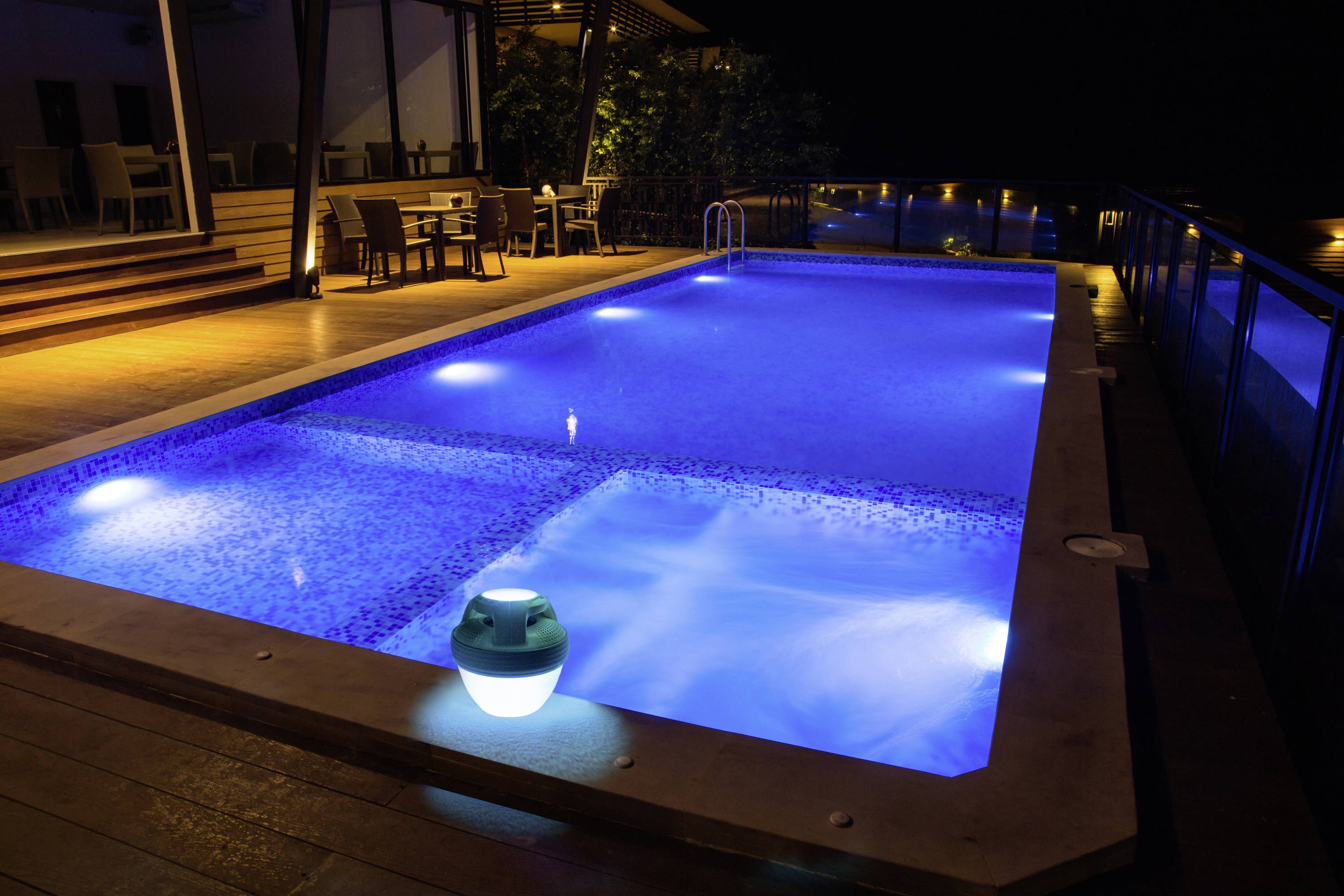 A lit swimming pool at night, surrounded by sun loungers and tables on a terrace, creates a relaxing atmosphere.
