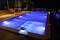 A lit swimming pool at night, surrounded by sun loungers and tables on a terrace, creates a relaxing atmosphere.