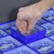 A hand takes a coin capsule out of a blue storage drawer. Several coin capsules are stored in the drawer.