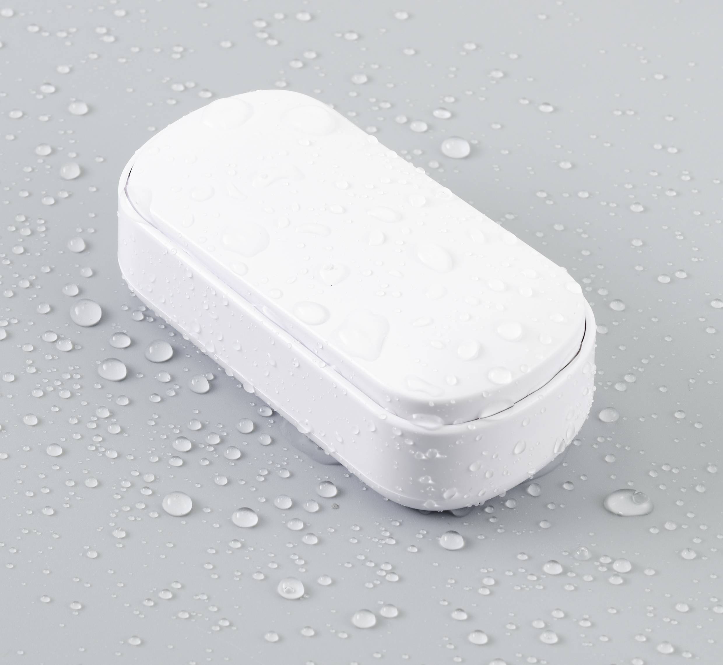 A white, rectangular device lies on a grey surface, covered in water droplets.