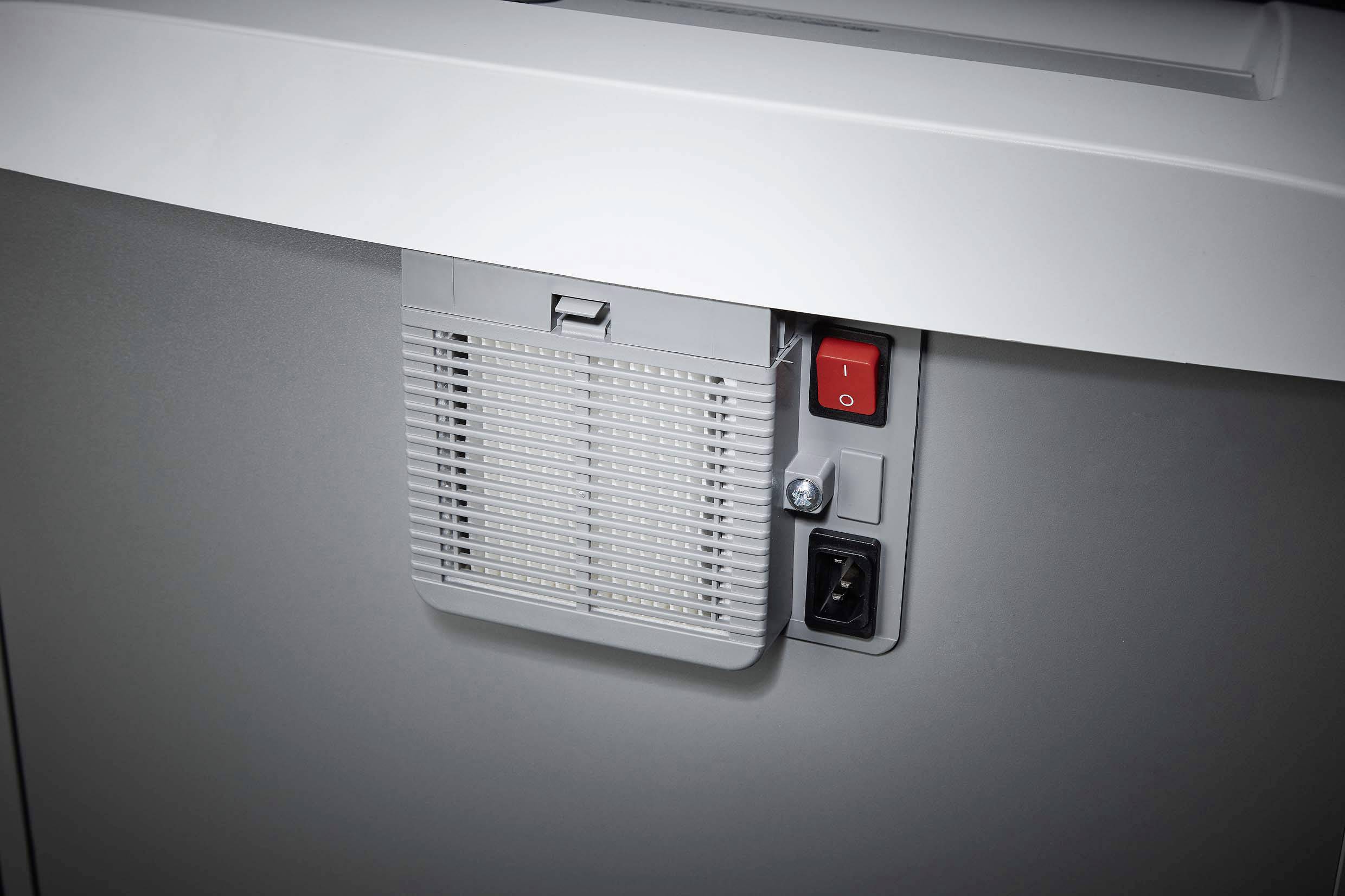 A grey shredder with a ventilation grille at the front. A red on/off switch is located in the top right corner.