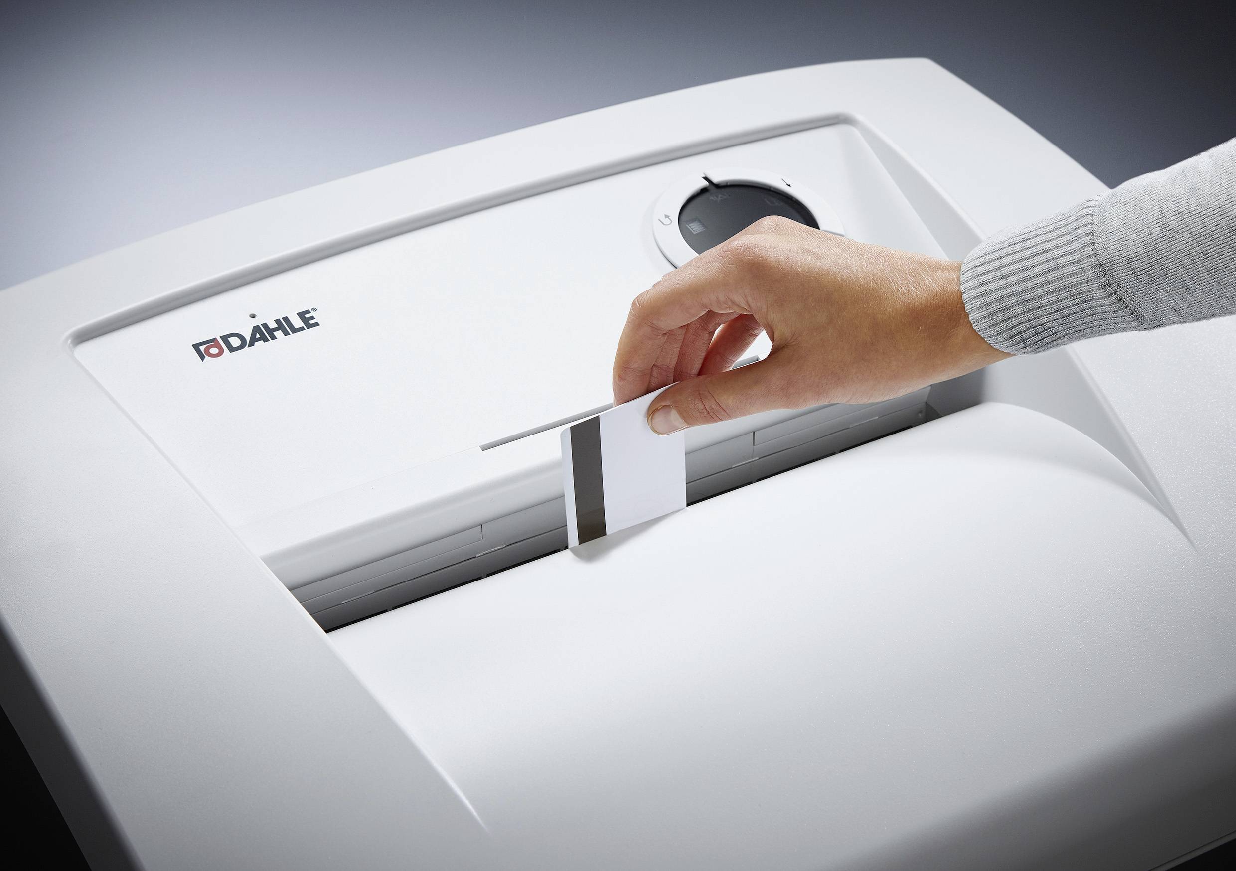 A hand is inserting a sheet of paper into a 'Dahle' shredder, ready to destroy the document.
