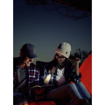 A man and a woman sitting cosily while camping outdoors. They are laughing and reading by lantern light in front of a tent.