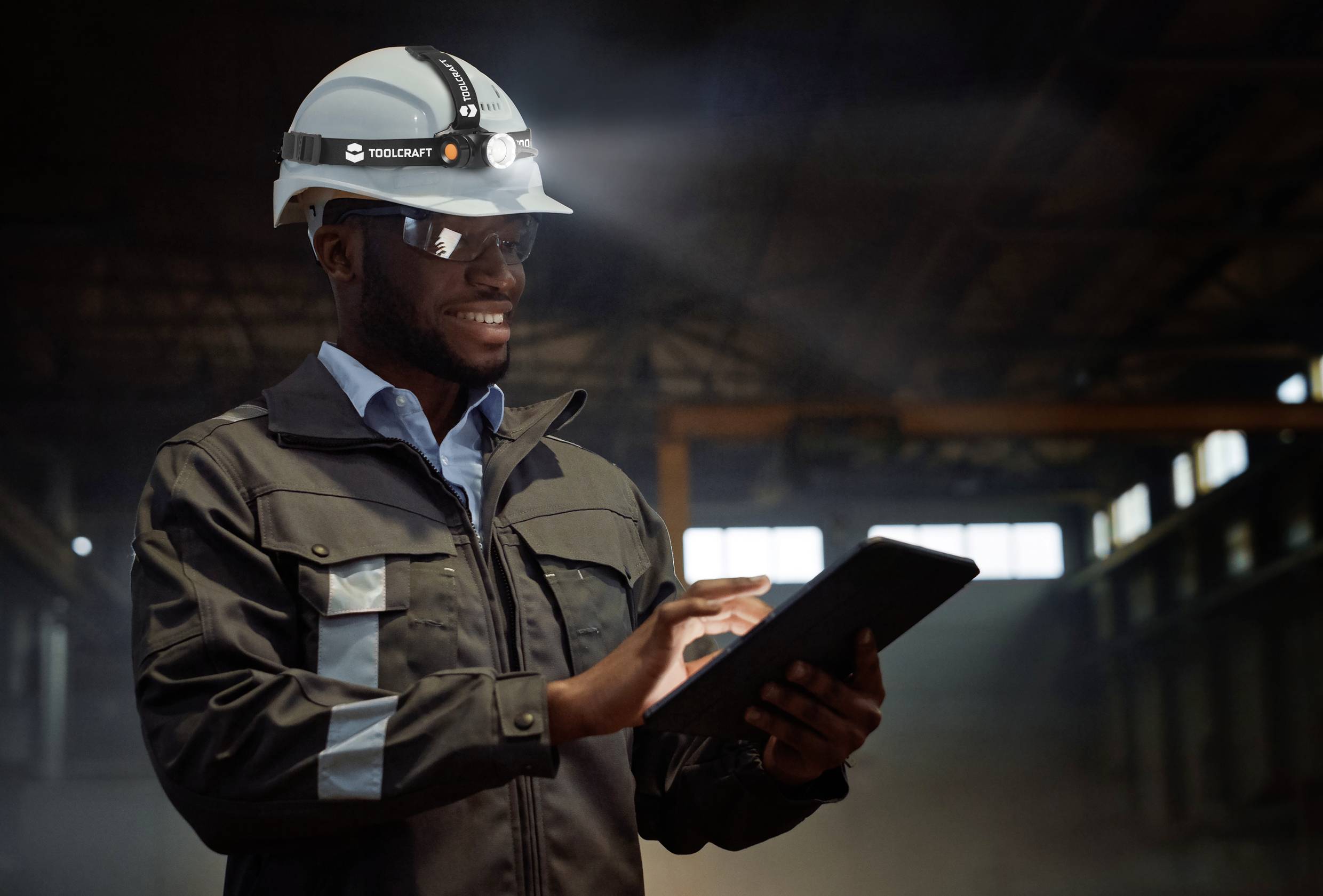 A person in work attire and a hard hat is using a tablet in an industrial setting, potentially for inspection or data collection.