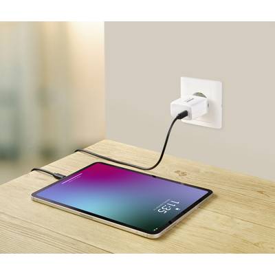 A tablet is lying on a table and being charged via a cable plugged into a socket. The screen displays the time 11:35.