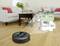 A robot vacuum cleaner is cleaning a living room with a wooden floor; next to it is a floor plan showing: living room, kitchen, dining room, entrance area.