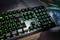 Illuminated mechanical keyboard with green LEDs on a desk. Arrow keys and function keys clearly visible.