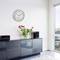 A contemporary interior design with a black chest of drawers, a floral arrangement in a vase placed on top, and a red wall clock.