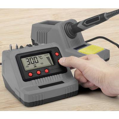 A person sets the temperature on a digital soldering station to 300 degrees Celsius. The station is positioned on a wooden table.
