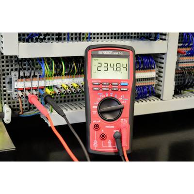 A digital multimeter is measuring a voltage of 234.84 V at an open electrical cabinet with multiple coloured cables and connections.