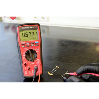 A multimeter is measuring the resistance of a component lying on the table. Display shows value: 0.6781.