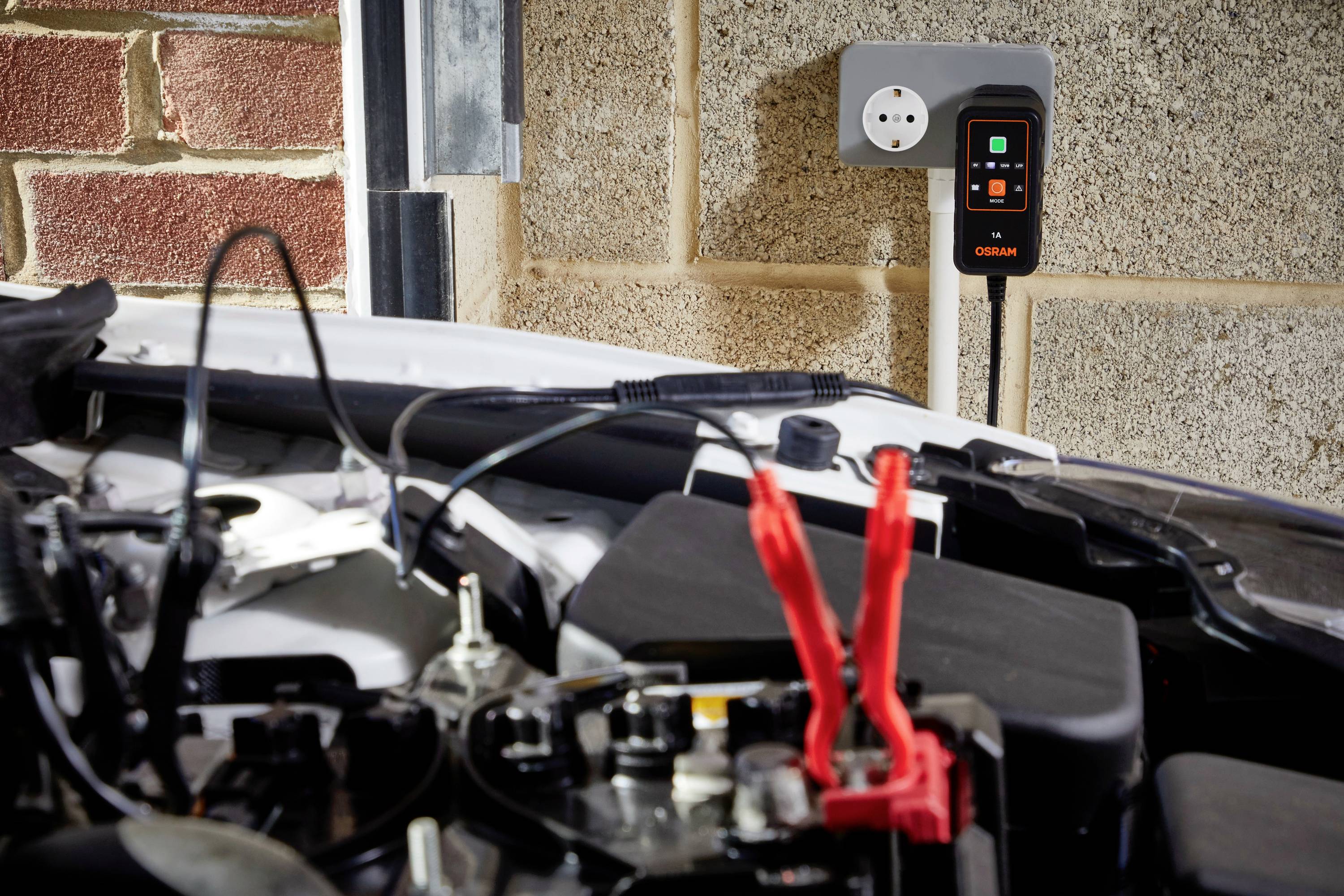 A car with its bonnet open is connected to a charging point. The charger is wall-mounted and in operation.