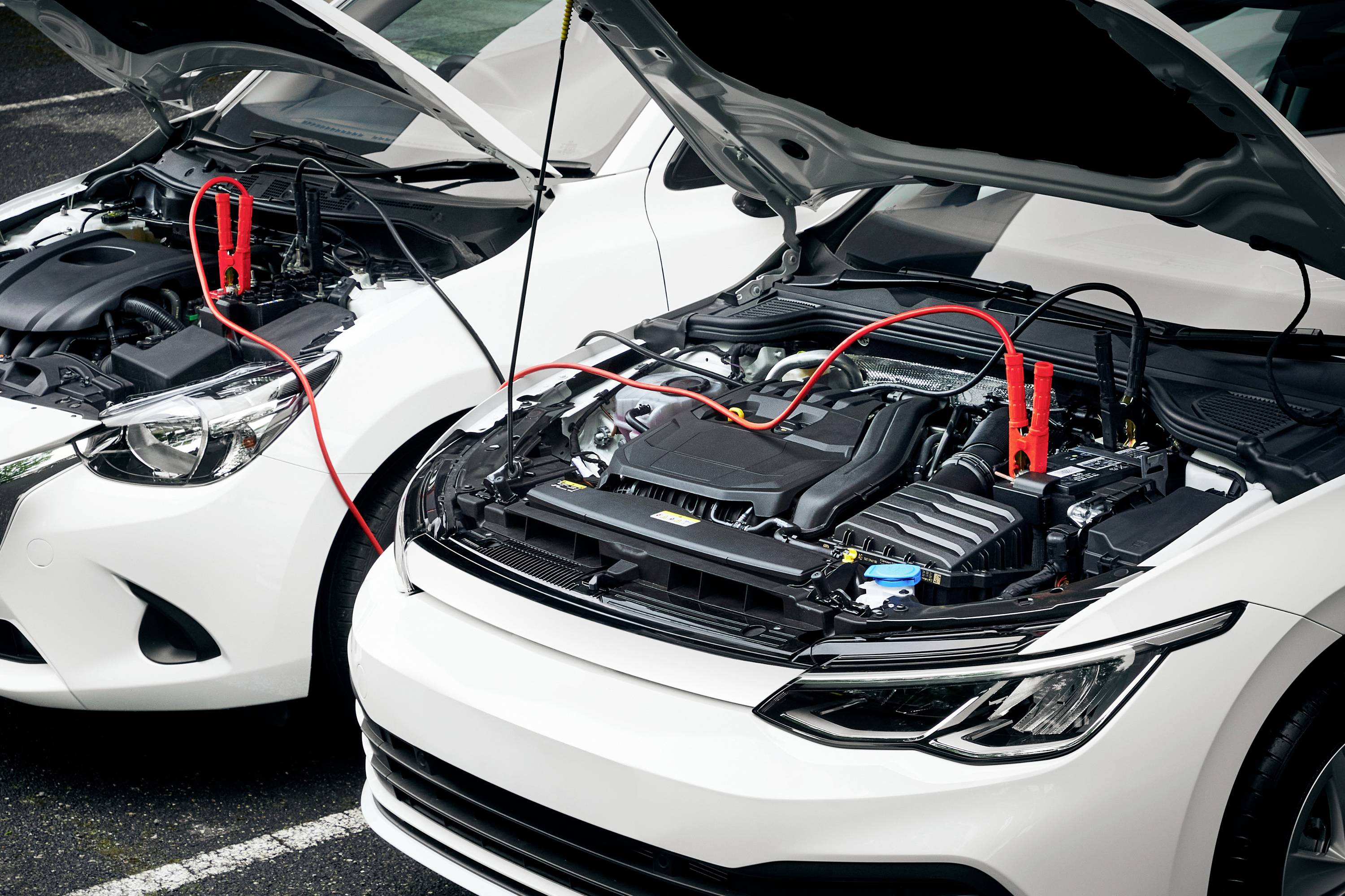 Two cars with open bonnets, connected by jump leads. One is donating, the other receiving energy through the cables.