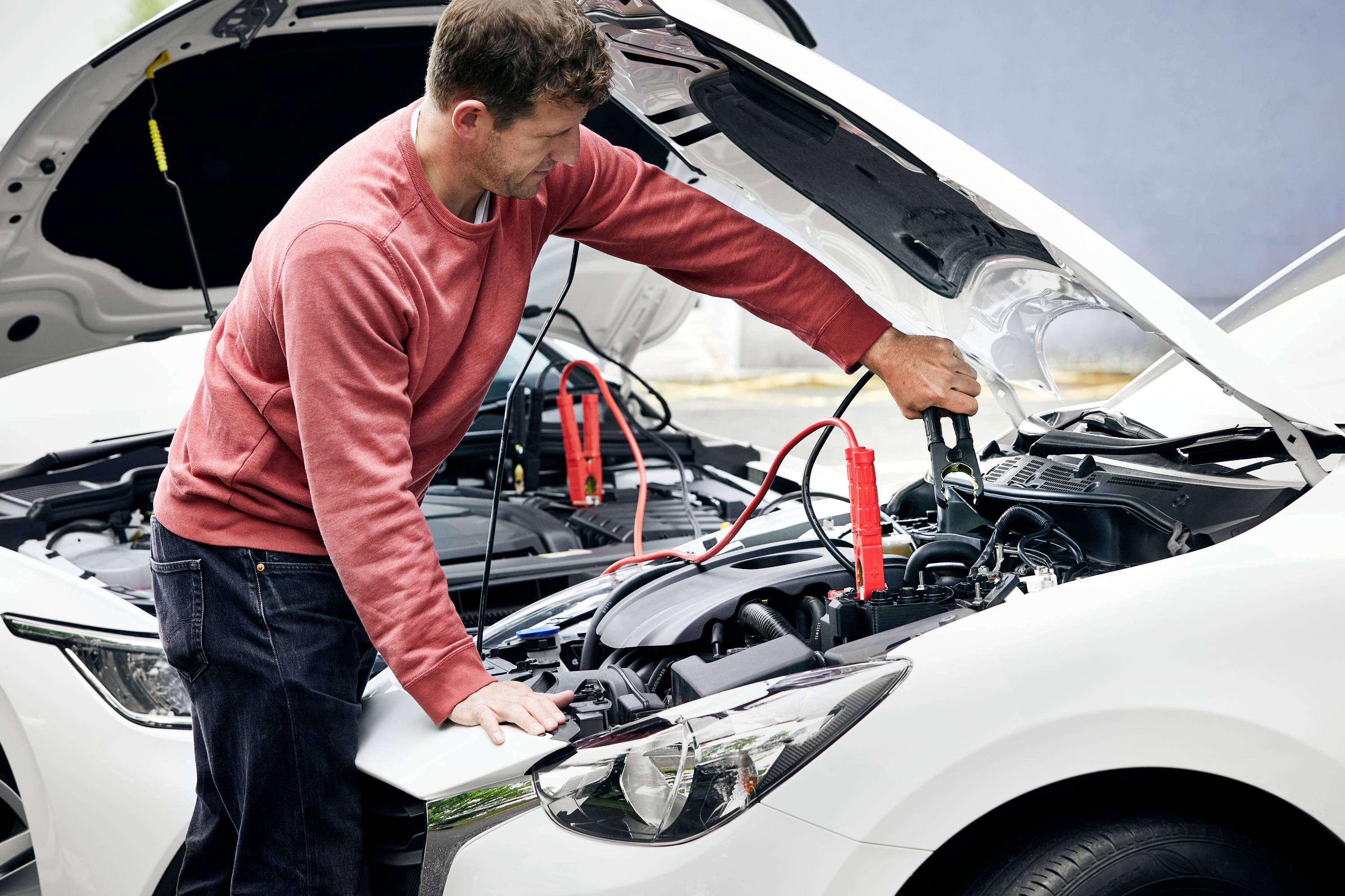 A man is jump-starting a car using jump leads and connecting the batteries of two vehicles.