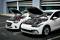 Two parked cars with open bonnets, connected by jump leads to assist with battery replacement.