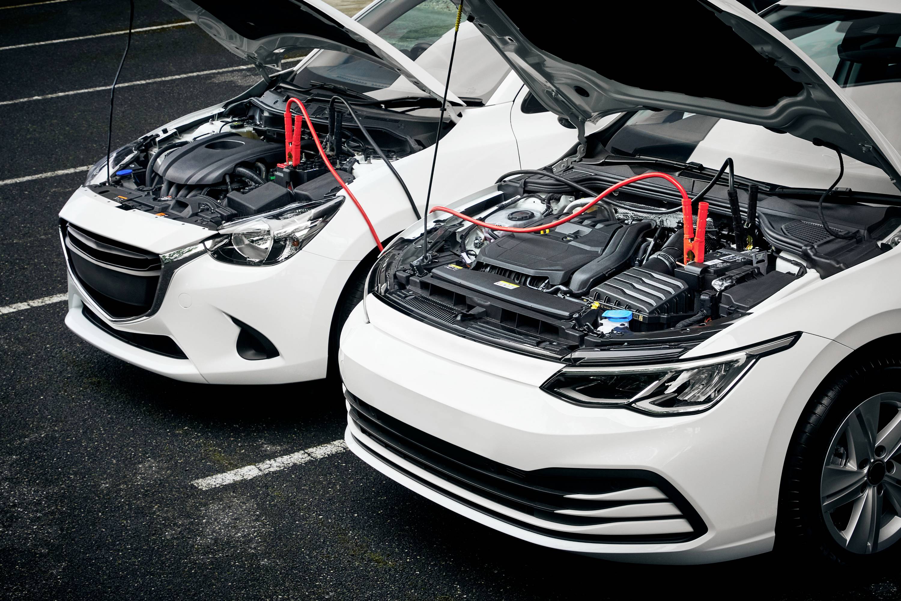 Two cars with open bonnets. Jump leads connecting the batteries. Breakdown situation on an asphalt road.