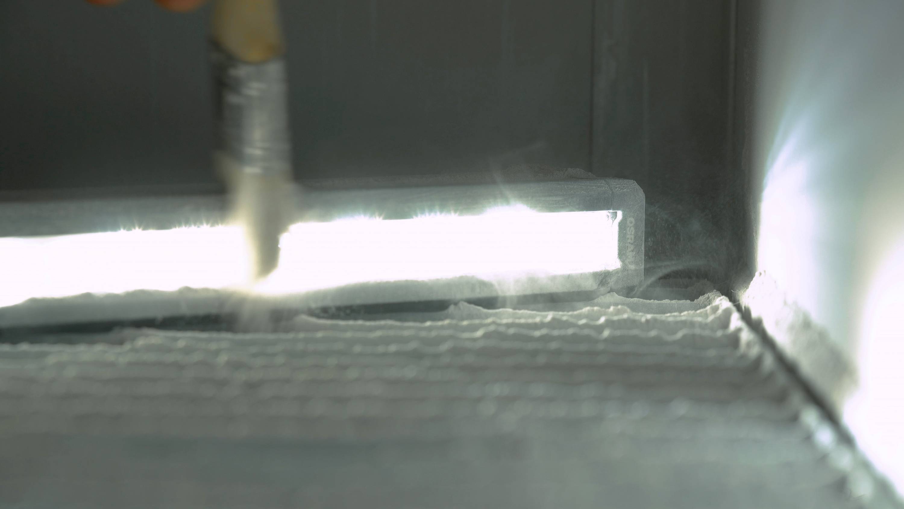 A brush touches a light surface, possibly a powder-coated surface, in an industrial setting.