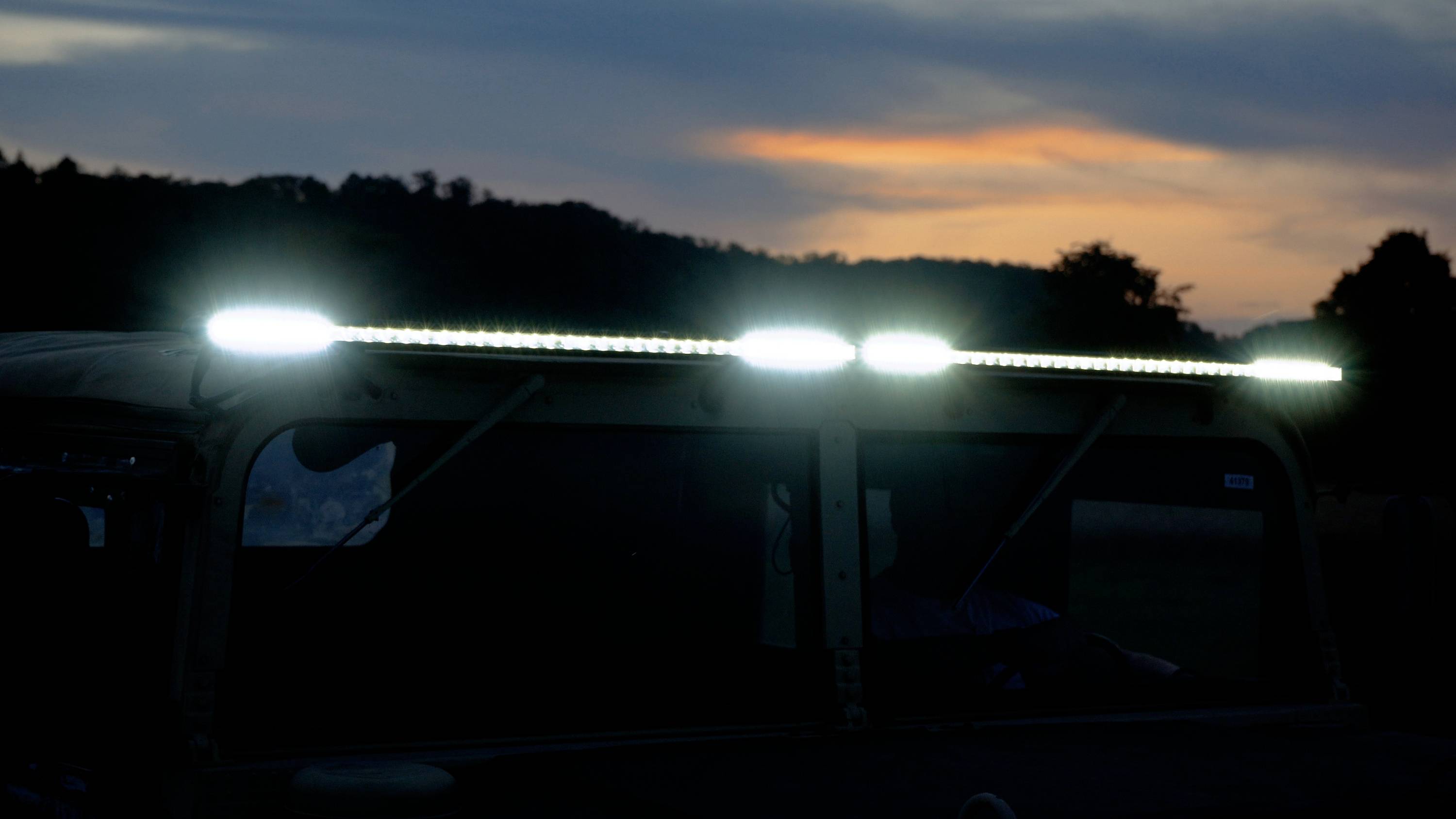 A vehicle roof with glowing LED lights at dusk against a wooded horizon.