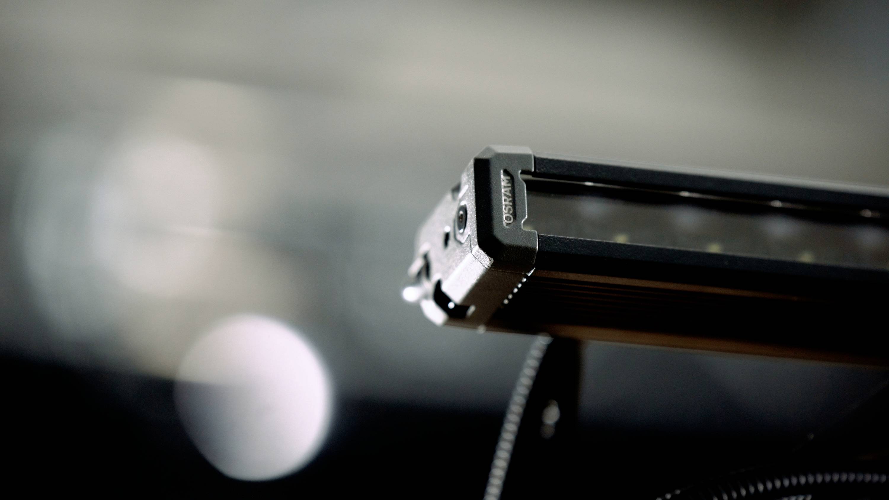 Close-up of an LED light bar with multiple lights, mounted on a black metal bracket. Blurred background.