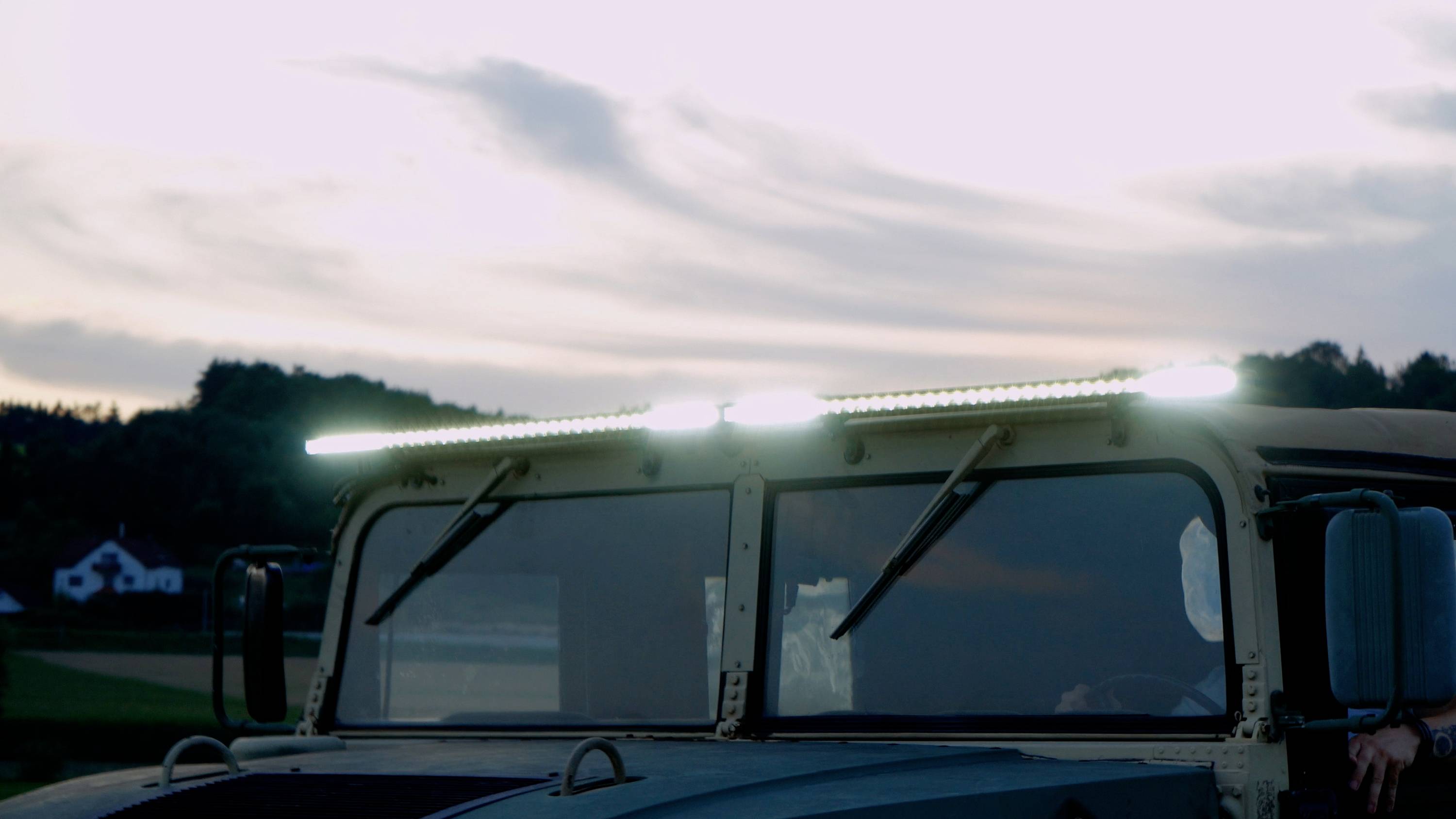 A vehicle with LED lights switched on mounted on the roof, outdoors at sunset. Trees are visible in the background.