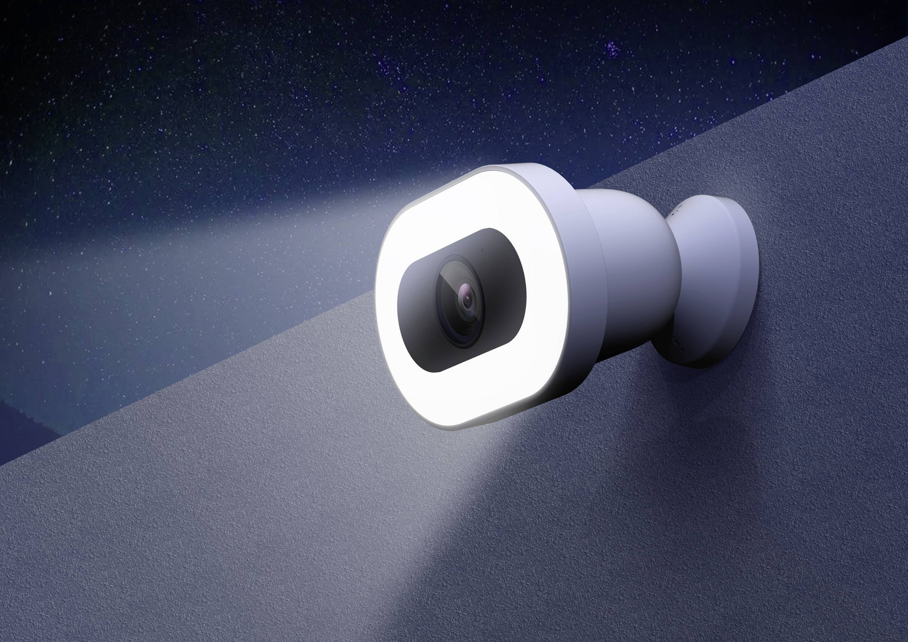 White surveillance camera with integrated light, mounted at an angle on a wall, projecting a bright light beam into the darkness.