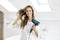 A woman with long hair is using a hairdryer in a modern, bright bathroom. She smiles contentedly.