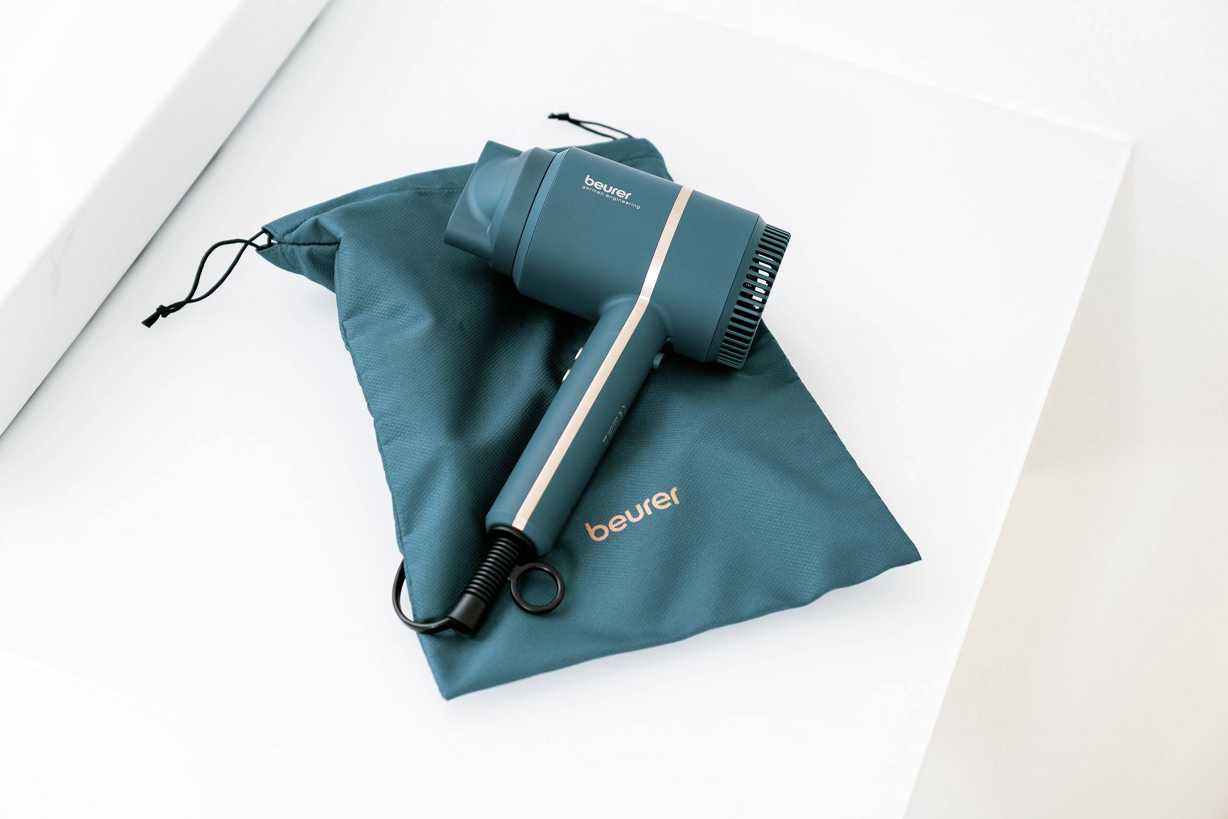 A turquoise hairdryer is placed on a matching fabric bag, both featuring the 'beurer' brand logo.