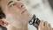 A man is shaving his chin with an electric razor. The background is out of focus.