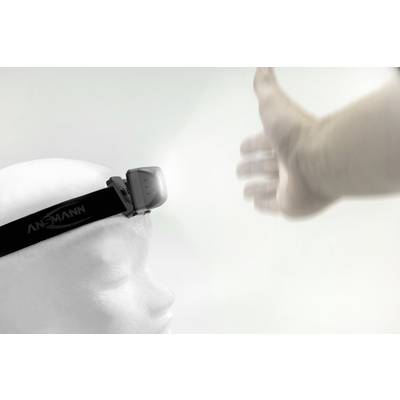 A white head with an ANSMANN head torch is illuminating an outstretched hand against a bright background.