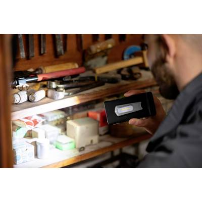 A man is holding a torch and illuminating a shelf with tools. Various tools and boxes are located on the shelf.