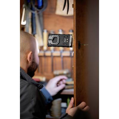 A man is working in a woodworking workshop. A black tool is attached to a door, with tools visible in the background.