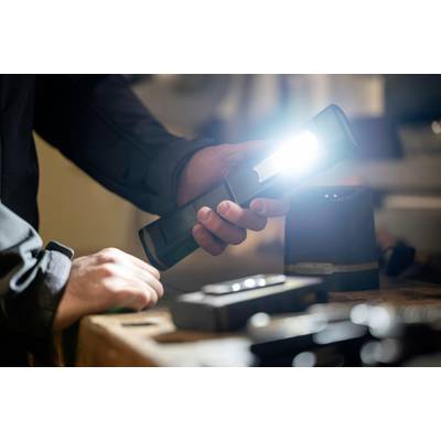 A person is holding a glowing torch in their hand, with tools lying on a workbench visible in the background.<br><br>Note: In British English, "flashlight" would be translated as "torch", and "workbench" is typically written as one word.