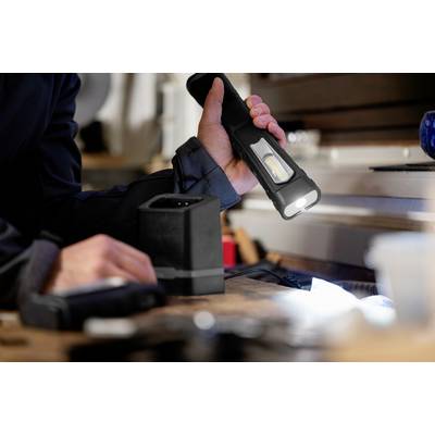 A person is holding a torch over a workbench in a workshop to illuminate an area.<br><br>Note: In British English, "torch" is used instead of the American "flashlight", and the translation maintains the original meaning and context of the sentence.
