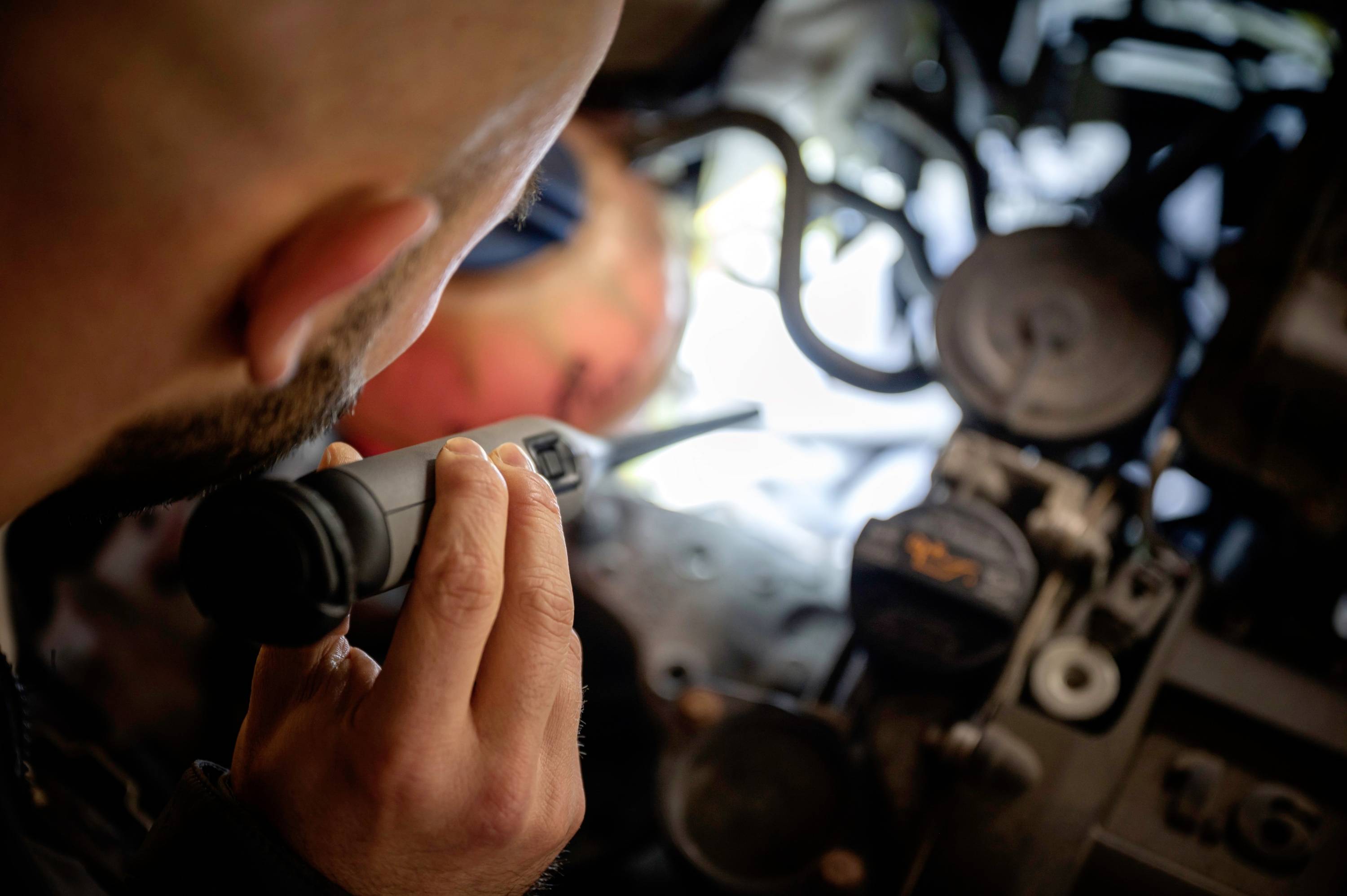 A person is inspecting the engine compartment of a car using an inspection camera. Various engine components and cables are visible.