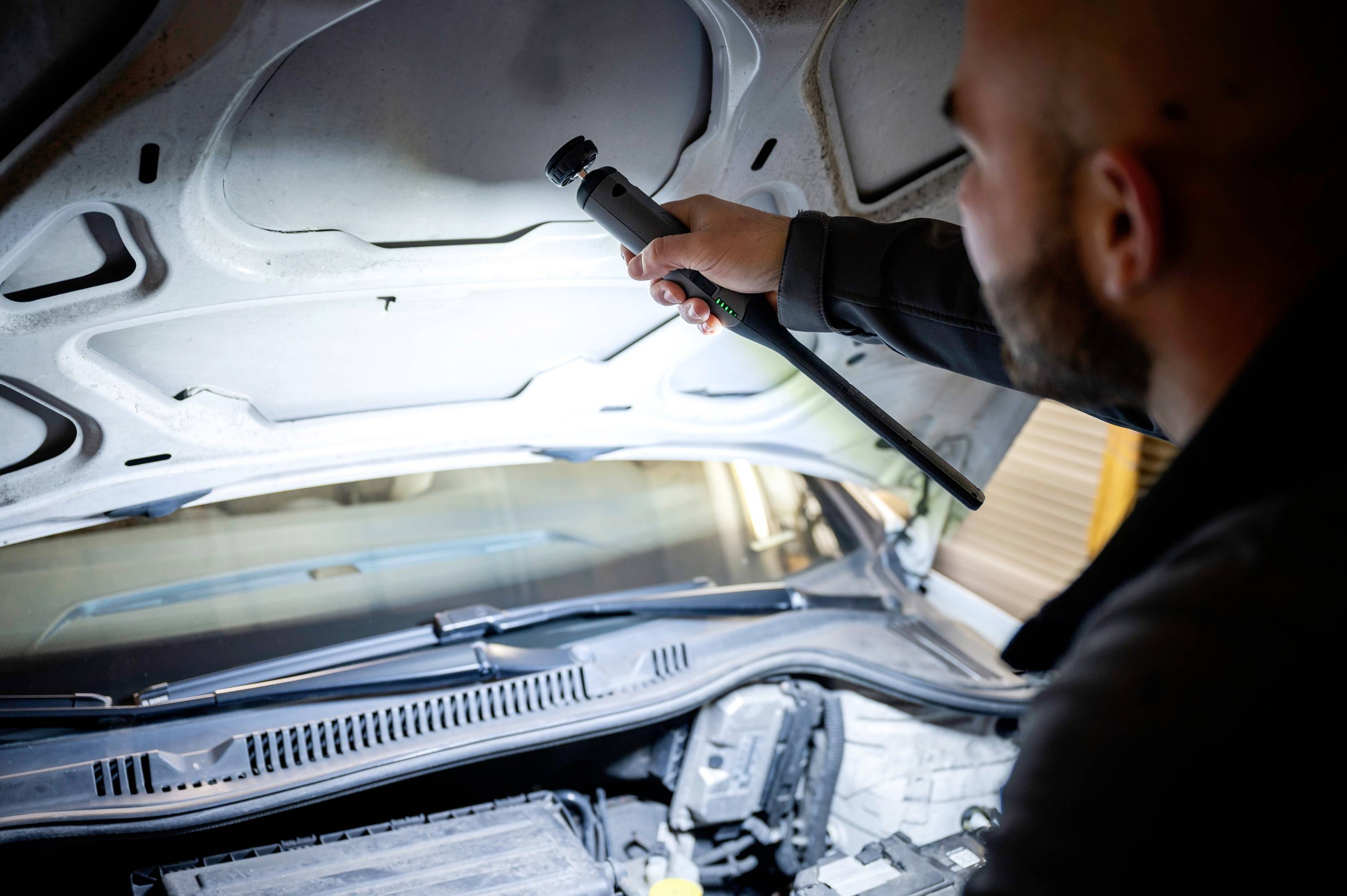 A person is examining the engine compartment of a car with a torch, possibly during maintenance or an inspection.