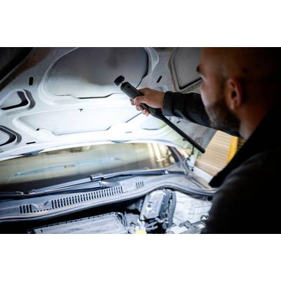 A person is examining the engine compartment of a car with a torch, possibly during maintenance or an inspection.